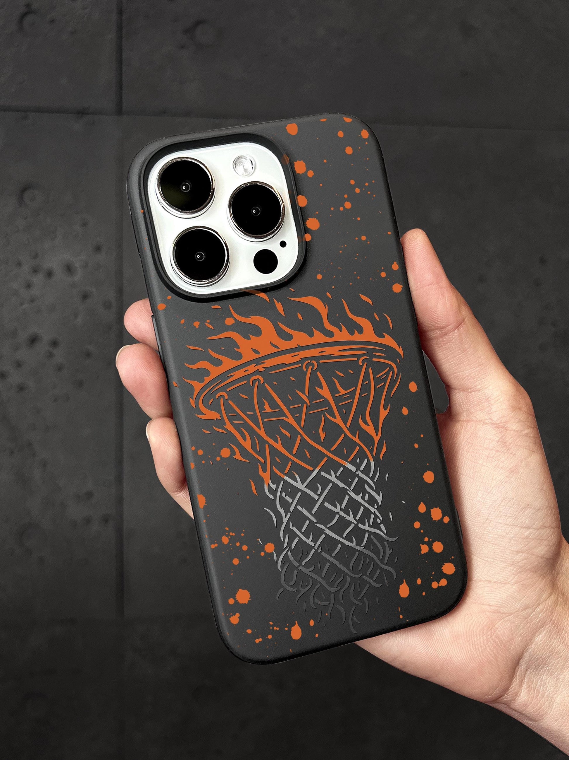 A person&#39;s hand holding a phone case with a basketball design featuring flames and a basketball net.