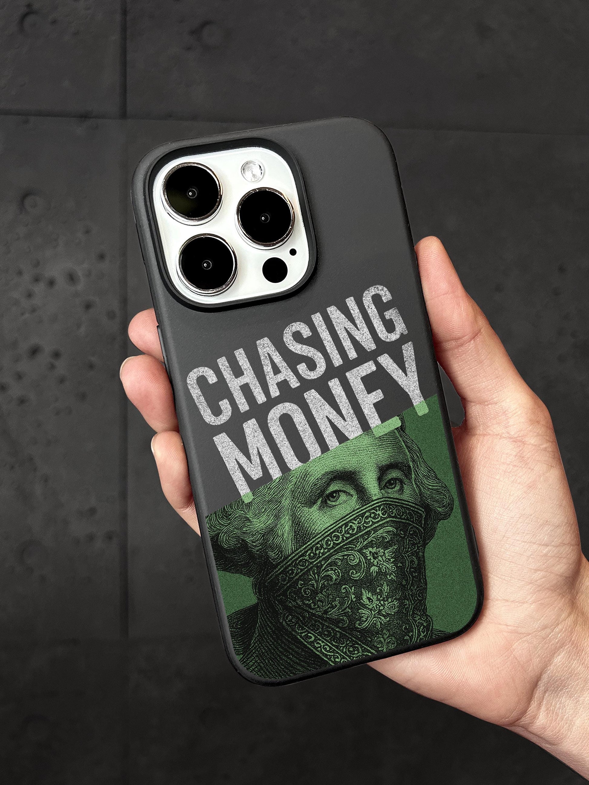A person&#39;s hand holding a black phone case with a design featuring a portrait of George Washington and the text &quot;CHASING MONEY&quot; printed on it.