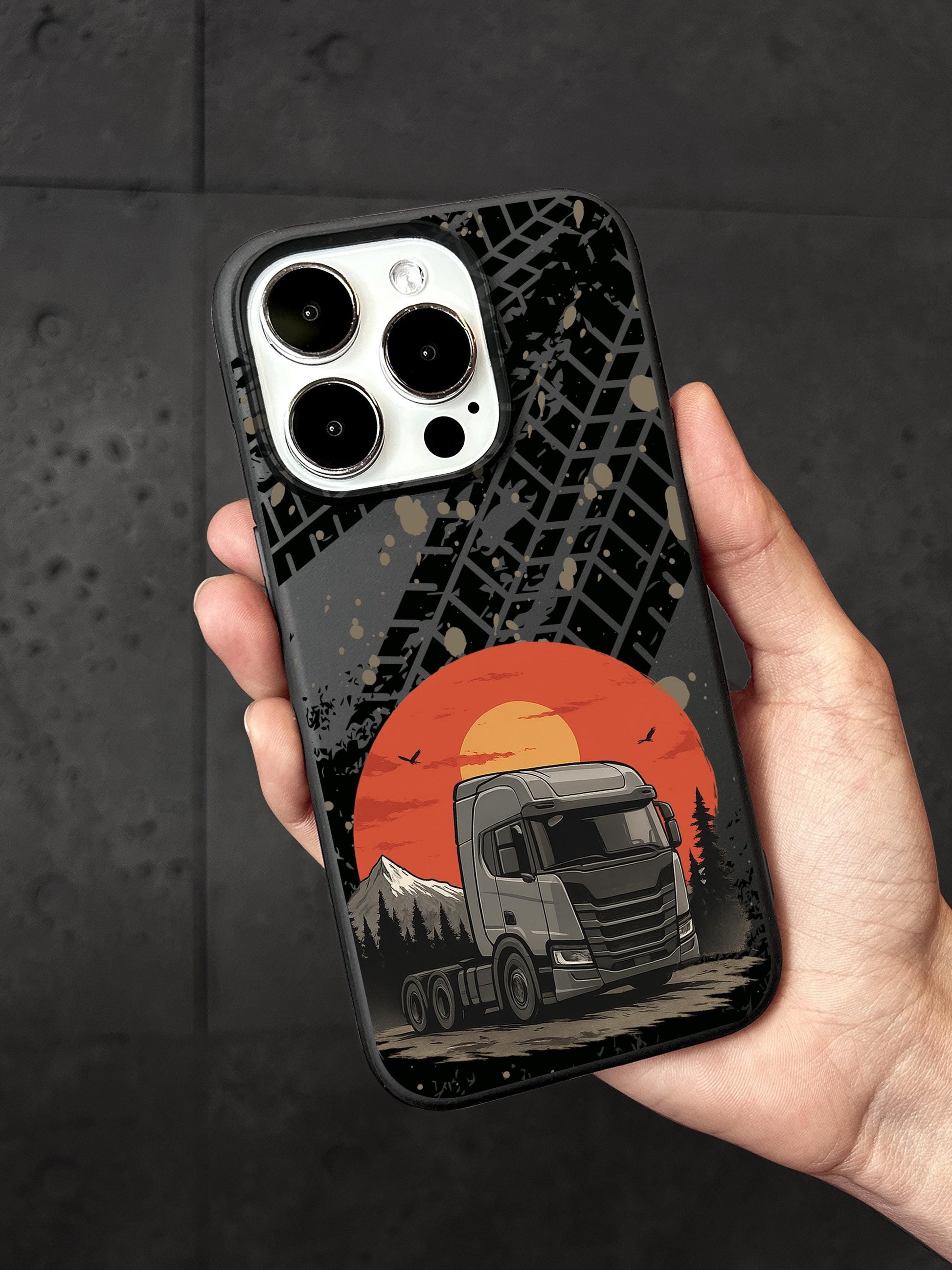 A person&#39;s hand holding a phone case with a design featuring a truck and a sunset landscape.