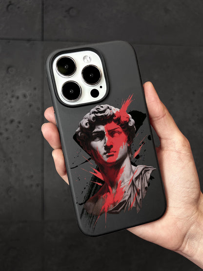 A person is holding a black phone case with a graphic design featuring a stylized portrait of a man&#39;s face, with splashes of red and black.