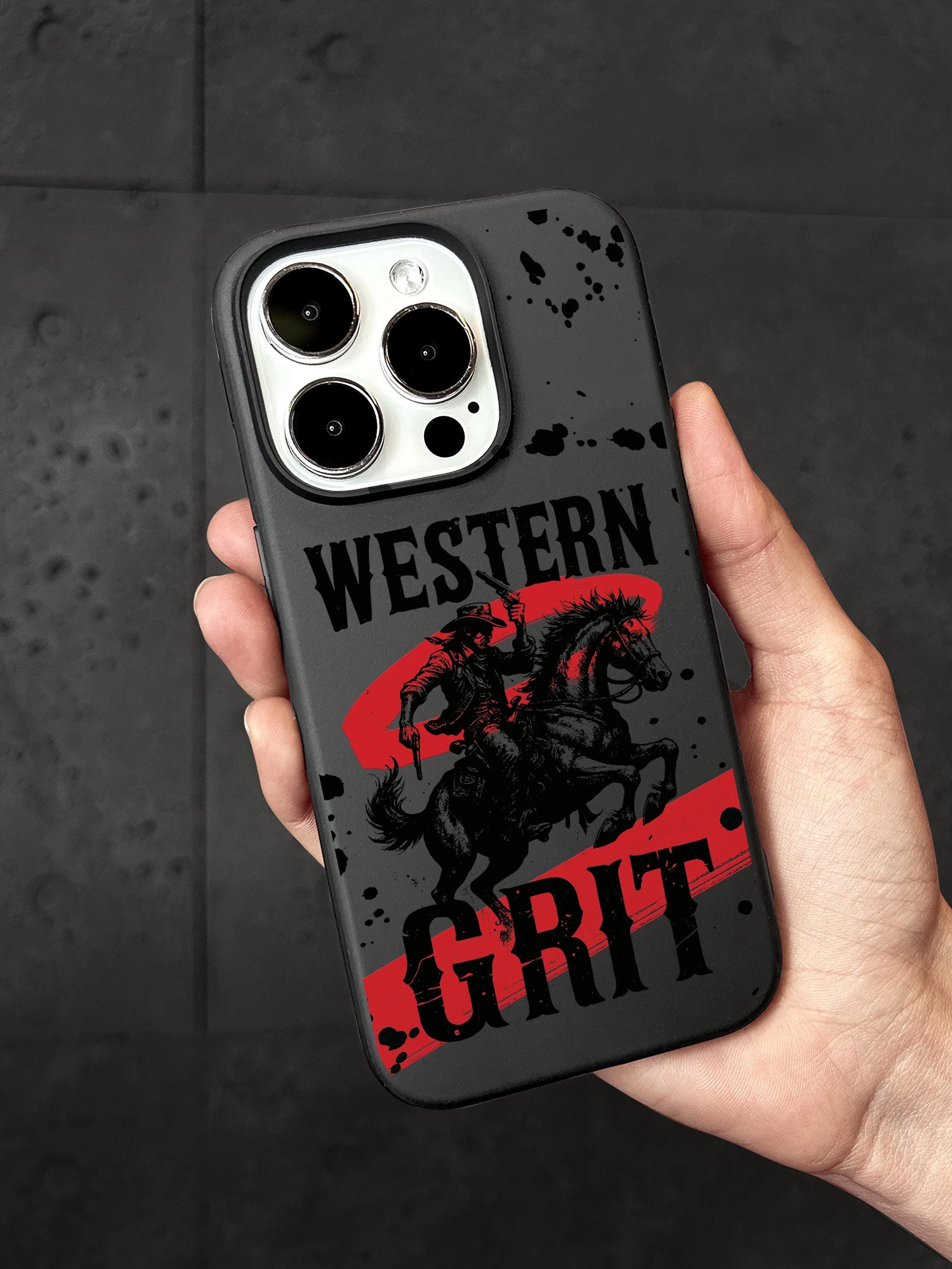 A person&#39;s hand holding a phone case with a graphic design featuring a cowboy on a horse and the text &quot;WESTERN GRIT&quot; printed on it.