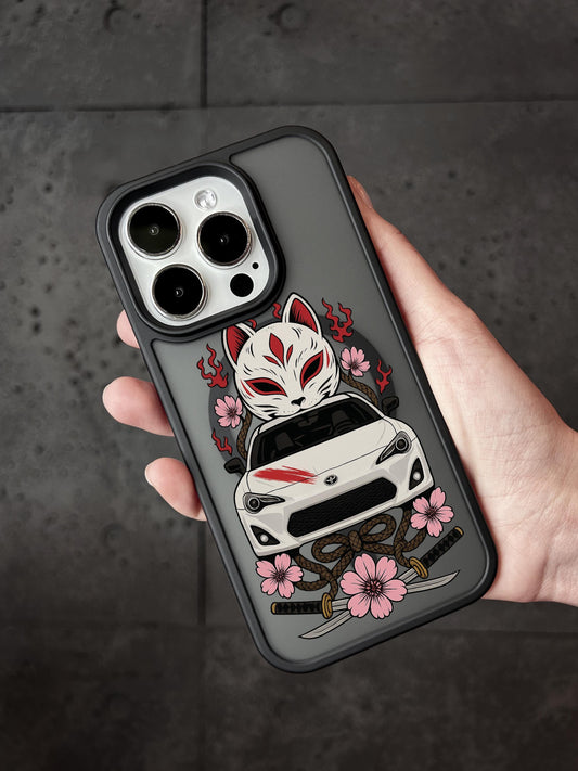 A person&#39;s hand holding a phone case with a design featuring a white car, a fox-like mask, and pink flowers.