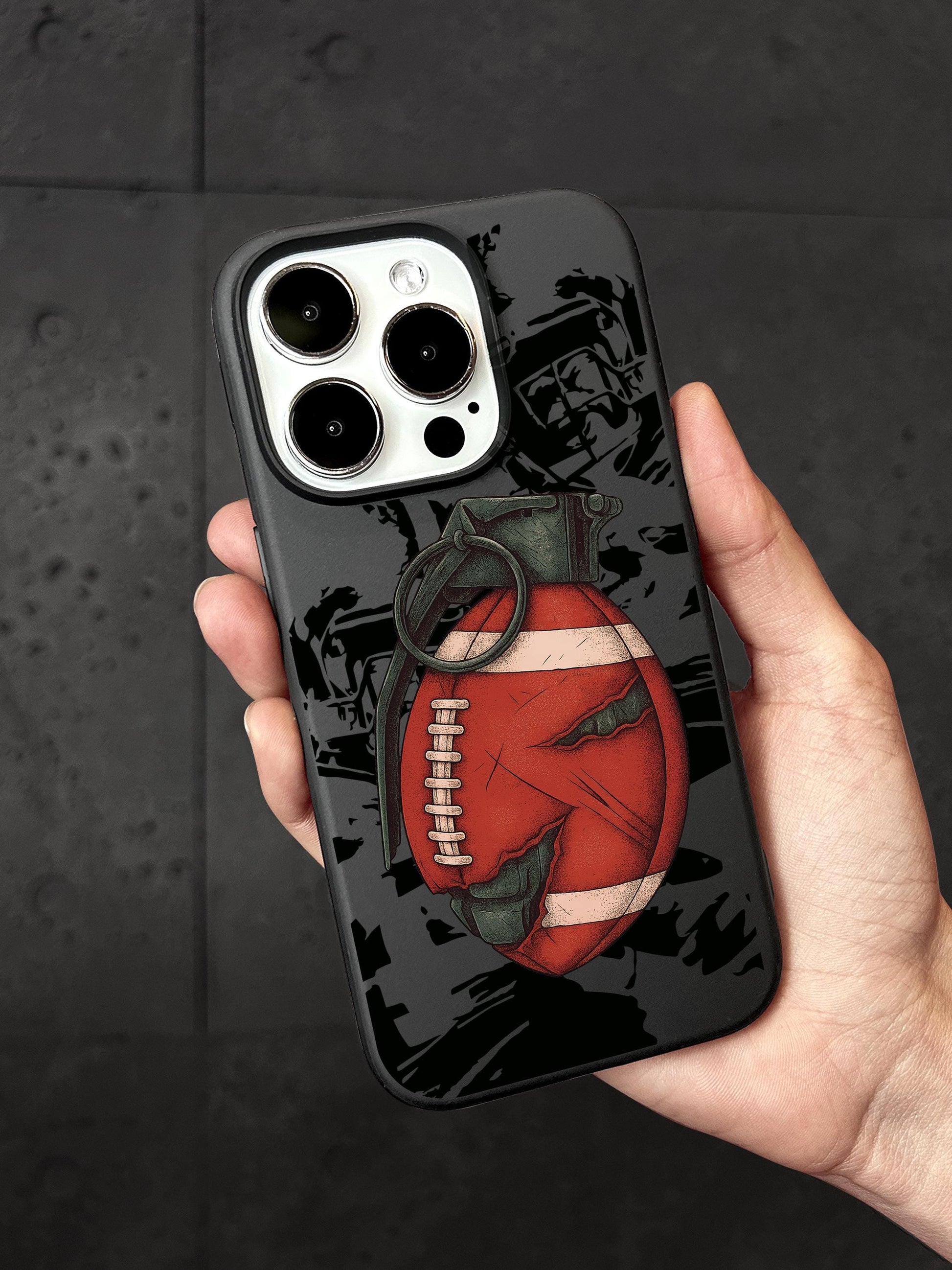 A person&#39;s hand holding a smartphone with a case featuring a graphic of a football and a bomb.
