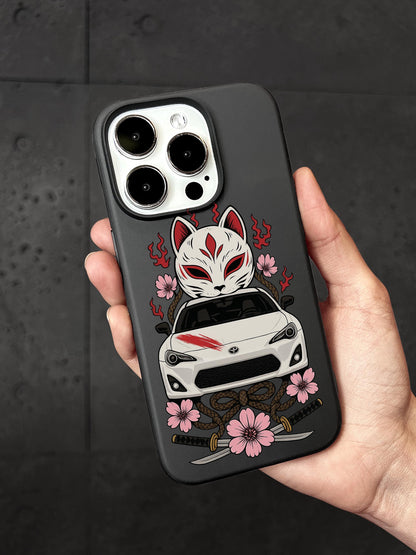 A person is holding a phone case with a design featuring a white car and a white cat with a red mask, surrounded by pink flowers and a sword.