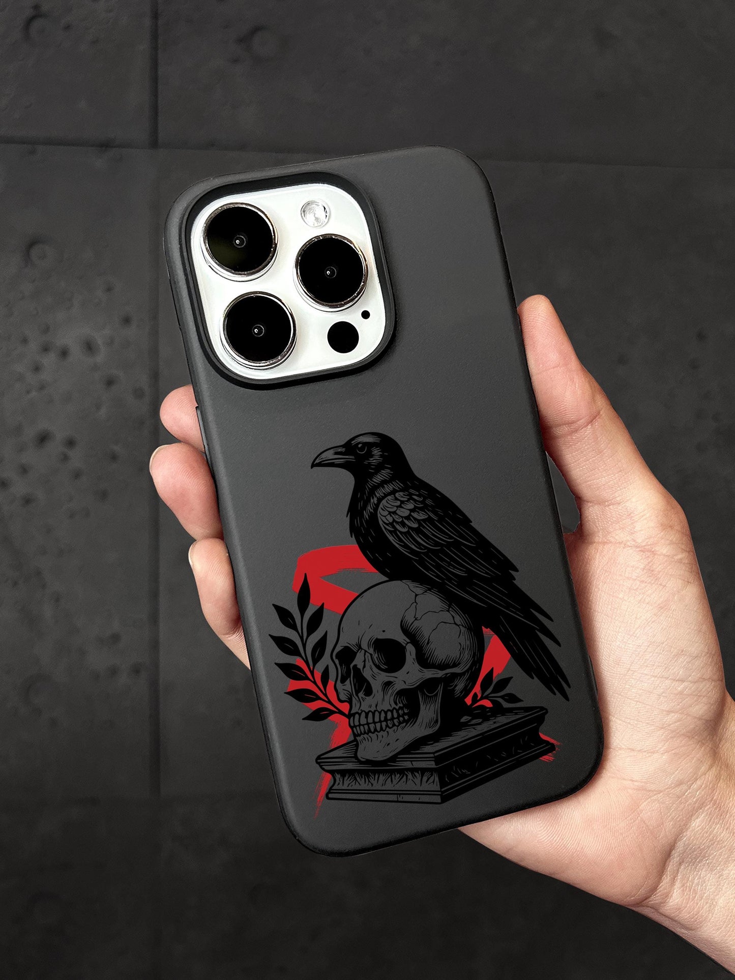 a person holding a phone case with a skull and a crow on it