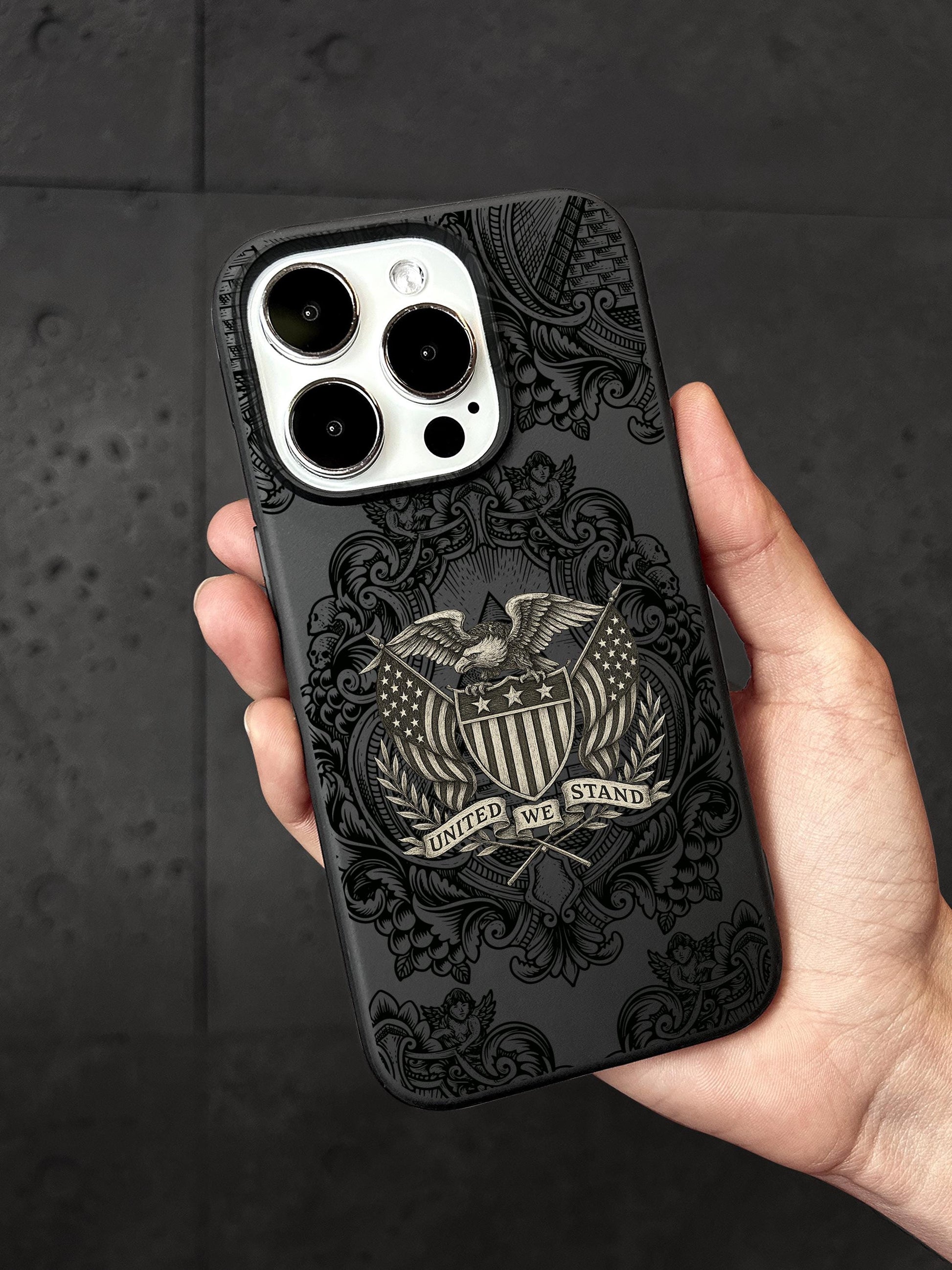 A person&#39;s hand holding a black iPhone case with a detailed design featuring an eagle and the text &quot;UNITED WE STAND&quot;.