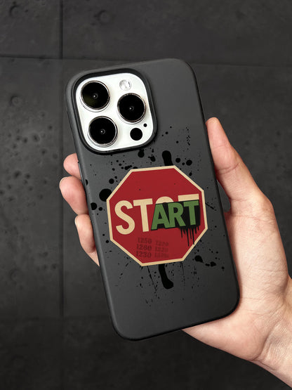 A person&#39;s hand holding a black phone case with a red stop sign sticker and the word &quot;START&quot; printed on it.
