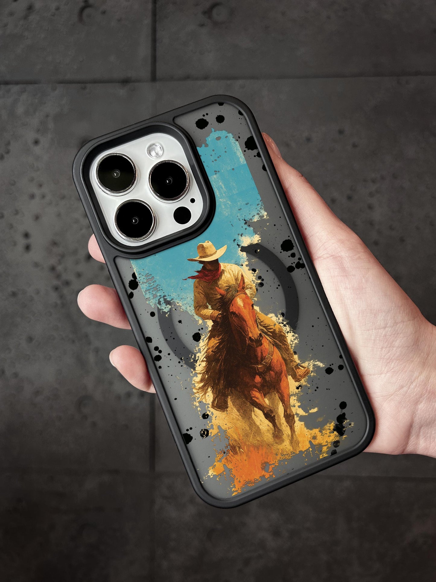 A hand holding a phone case with a cowboy riding a horse printed on it.