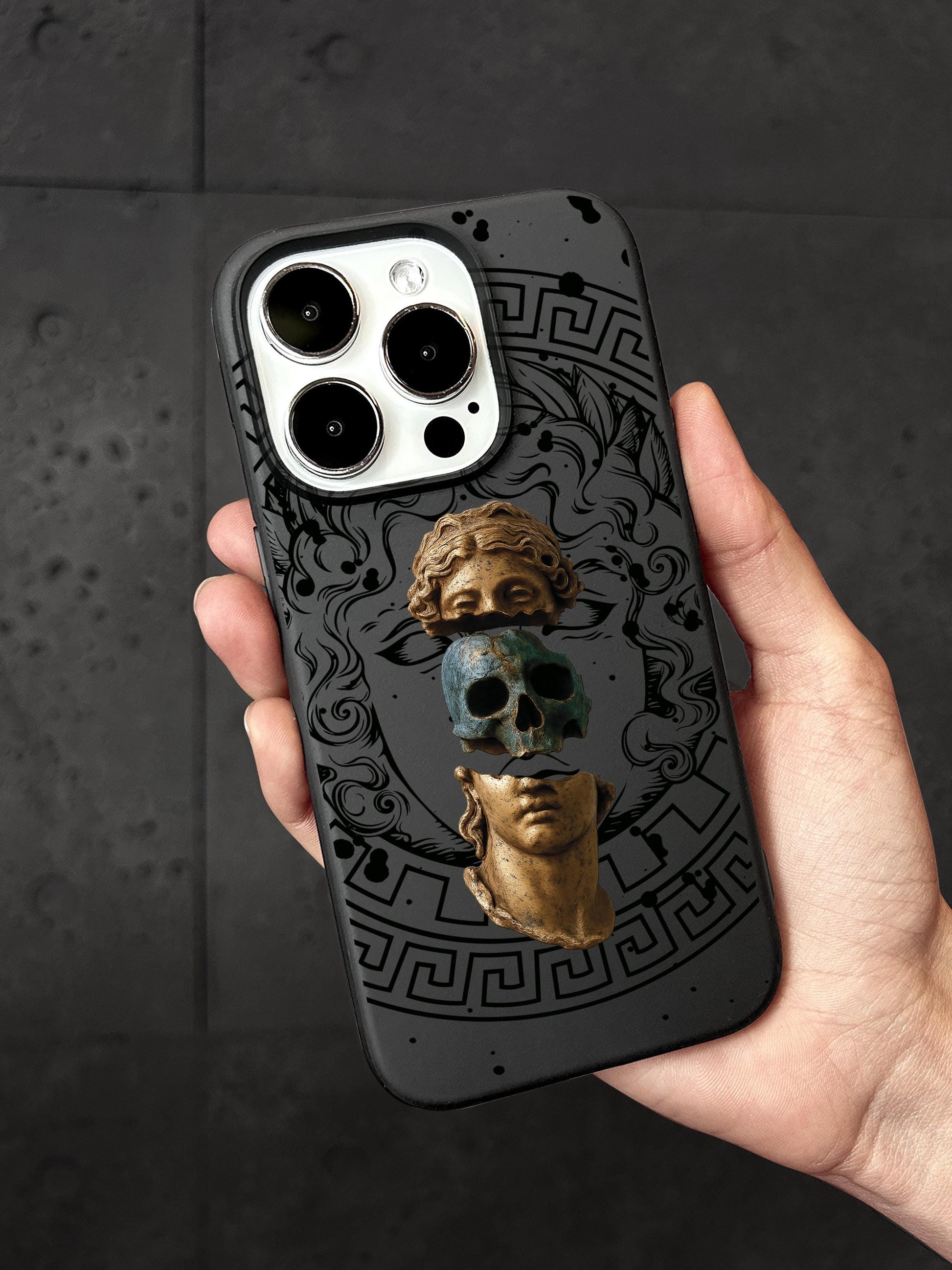 A person&#39;s hand holding a phone case with a design featuring a skull and a golden statue.